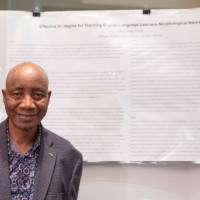Literacy studies faculty member, Dr. Nagnon Diarrasouba, standing in front of literacy studies graduate student, Maximilian Young's, poster.